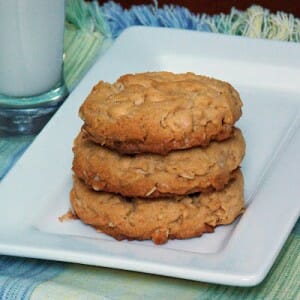 A stack of 3 peanut butter oatmeal cookies on a white plate with a small glass of milk behind the plate.