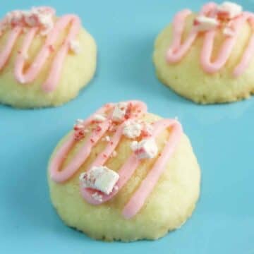 Peppermint Meltaway cookies with a pink peppermint glaze drizzle and crushed peppermint candy topping on a blue plate.