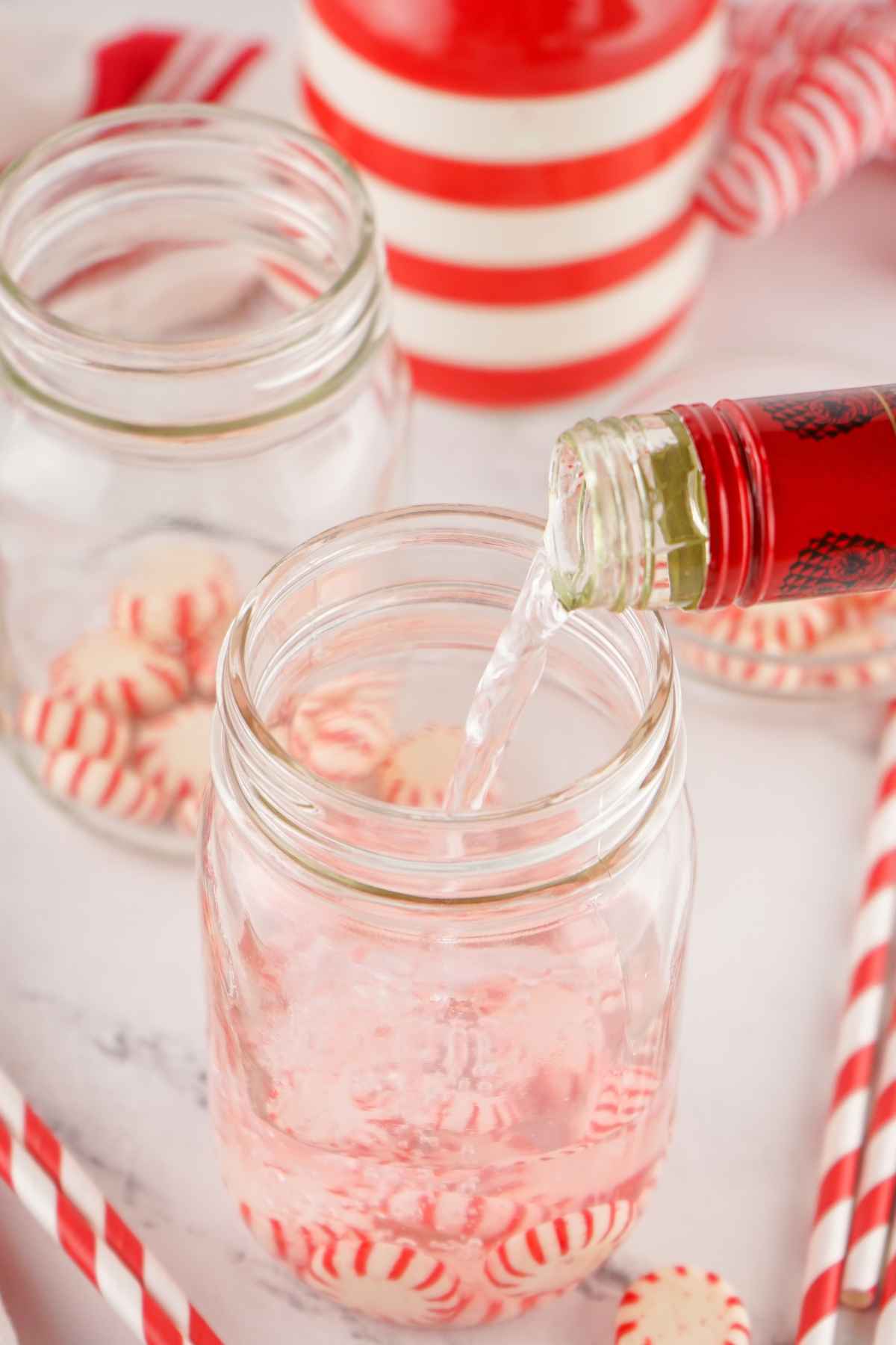 Pouring liquid into a clear mason jar filled with red and white candies.