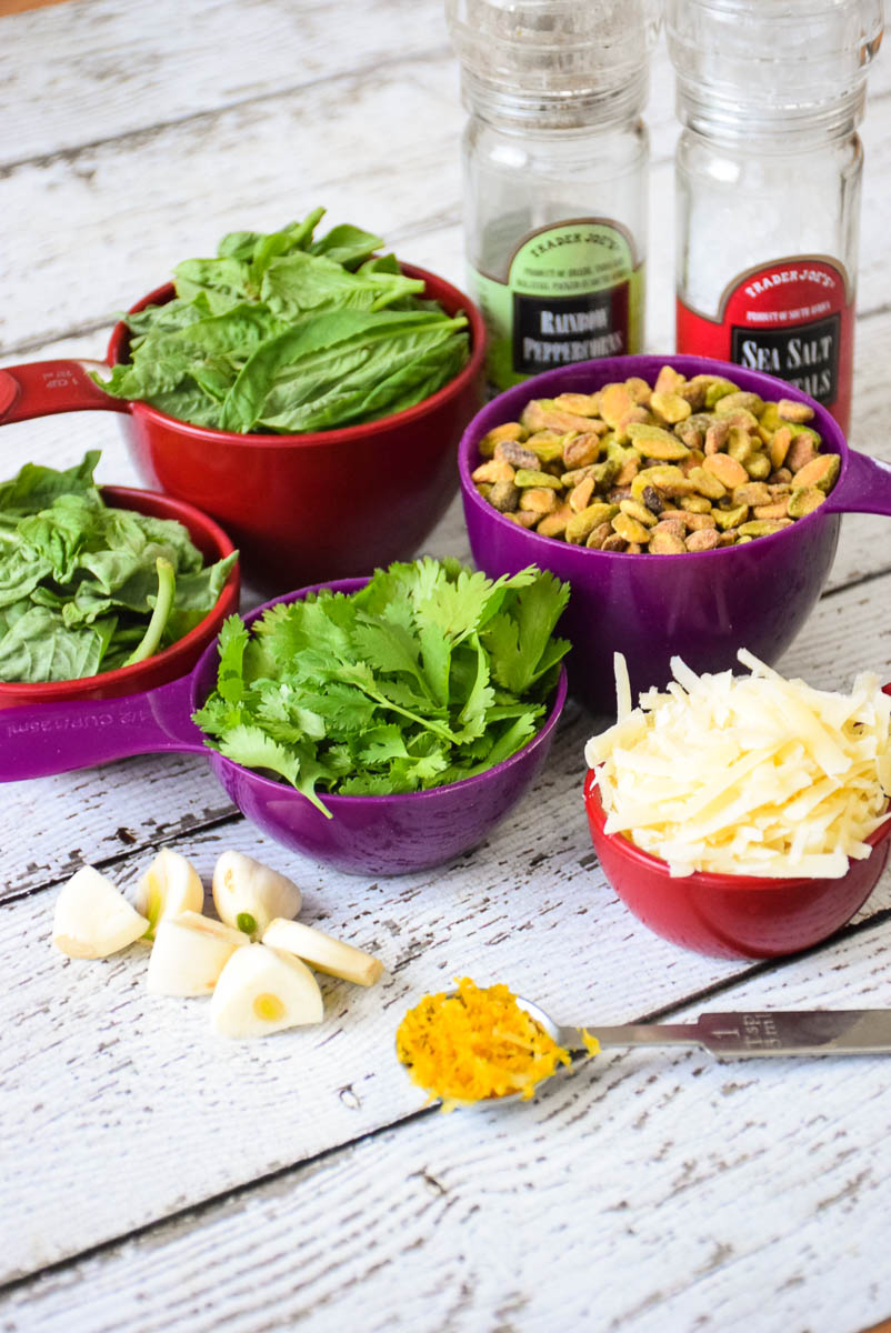 Fresh basil, parsley, roasted pistachios, cheese, garlic cloves, and seasonings mis en place.