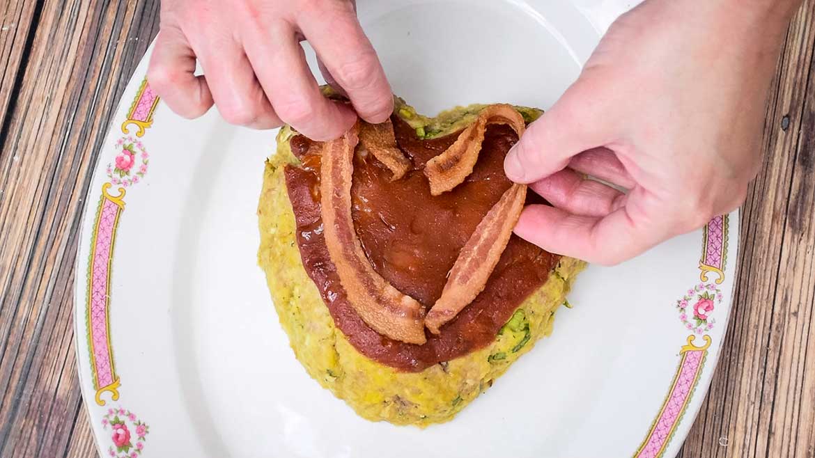 Placing the cooked bacon on the baked heart shaped veal meatloaf.