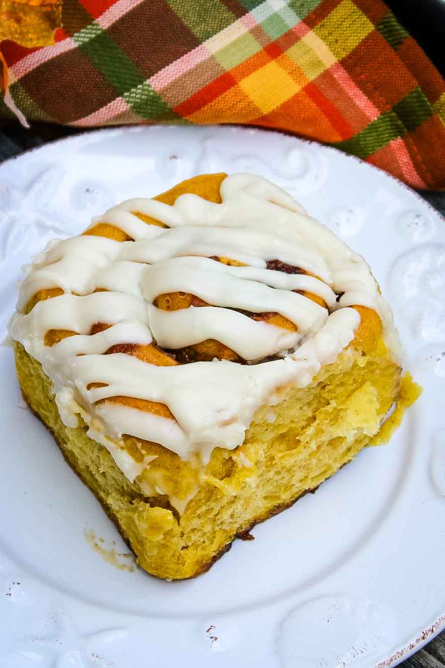 Baked Pumpkin Cinnamon Roll on a plate with an orange and green napkin next to it.