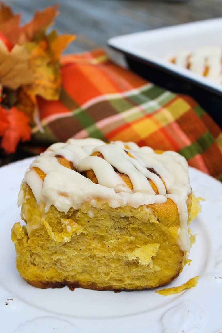 Pumpkin Spice Cinnamon Rolls on a white plate with a orange, green, and yellow checked napkin in the background.