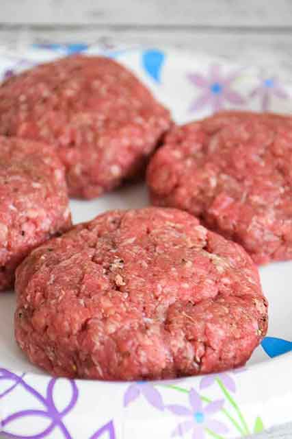 raw shaped ground hamburger steaks on a paper plate