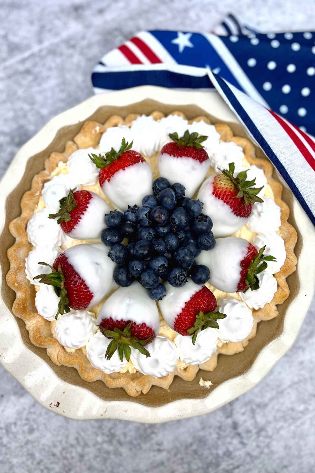 Overhead image of red white and blueberry pie decorated with white chocolate coated strawberries.