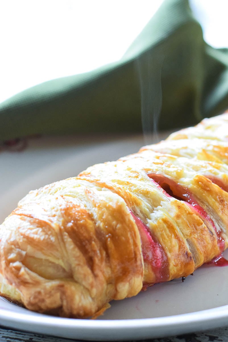 Whole baked rhubarb cheese danish on a white tray with steam rising out of the danish.
