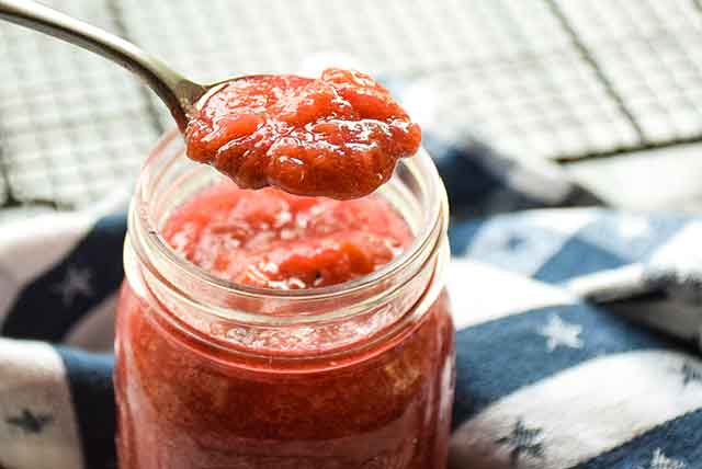 A glass jar full of rhubarb sauce and a spoonful of sauce above the jar.