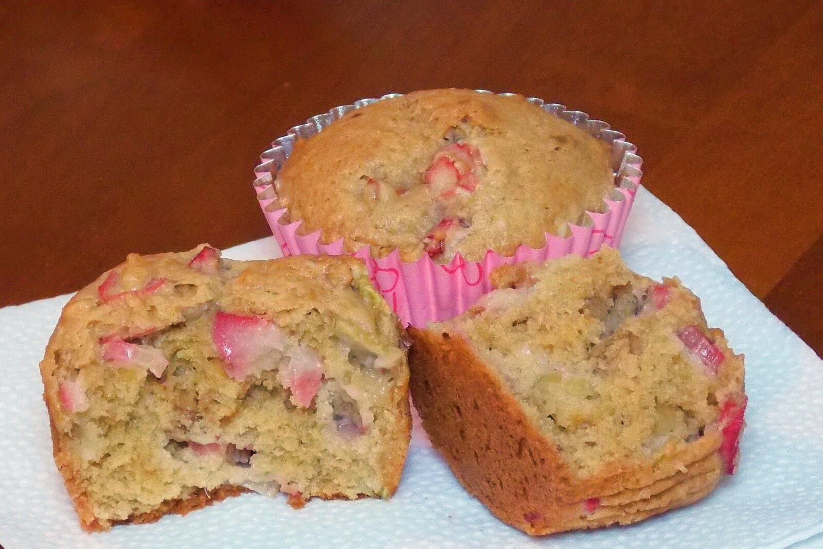 One rhubarb walnut muffin cut in half on a white plate with a whole muffin in the background.