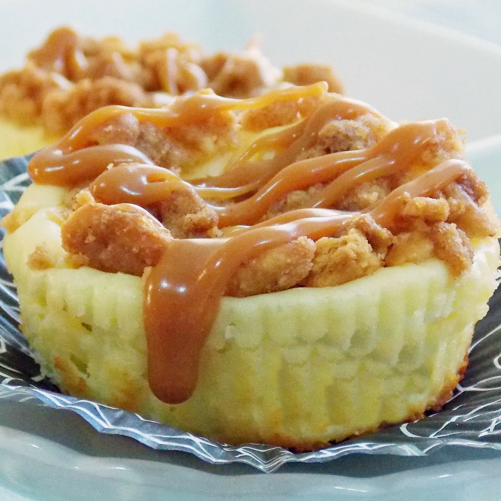 Baked mini cheesecake with a crumb topping and caramel drizzle.