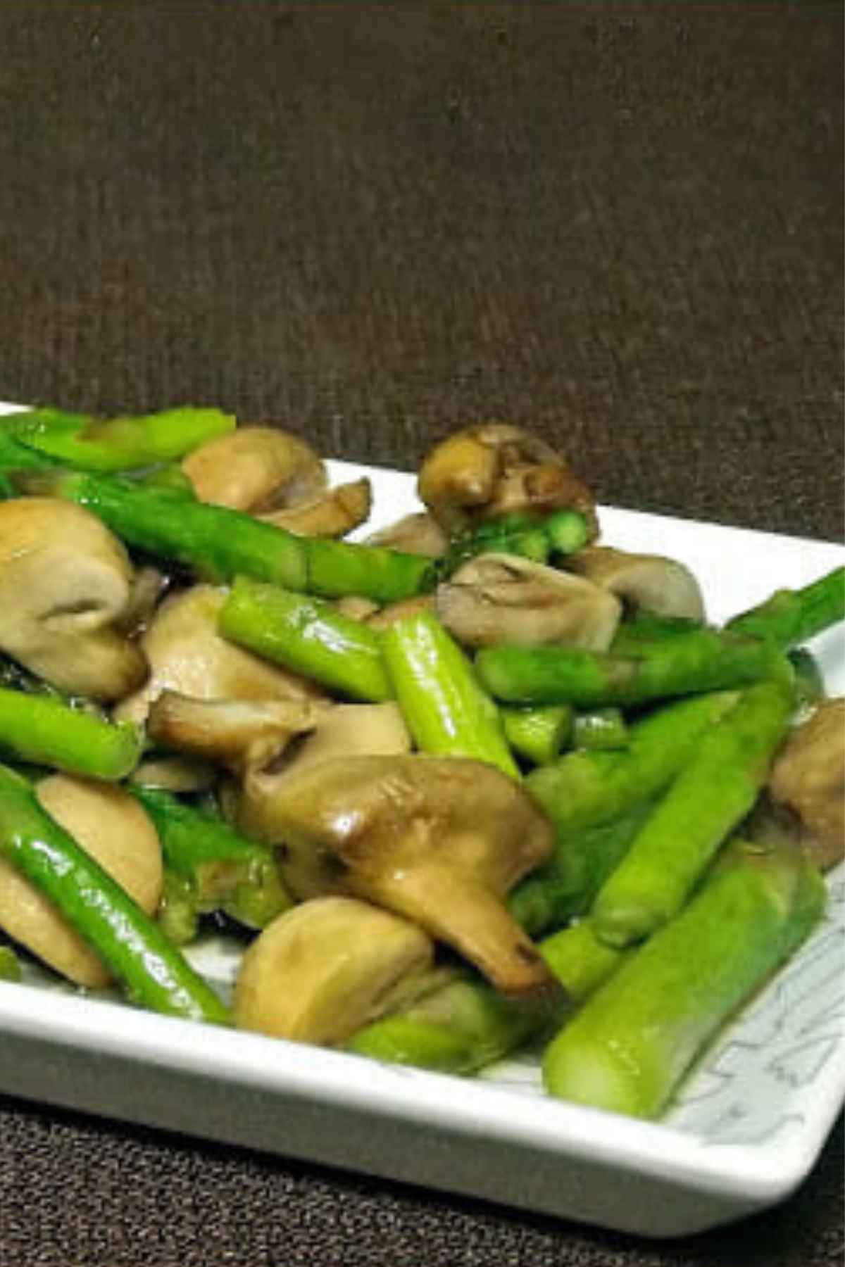 A white serving tray with roasted asparagus and mushrooms inside the tray.