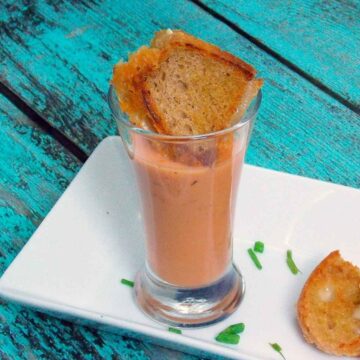 featured image roasted tomato soup shooter on a white plate with mini toasted brie cheese croutons