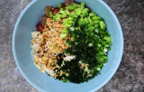 A blue mixing bowl with all of the salad ingredients in it before being mixed.