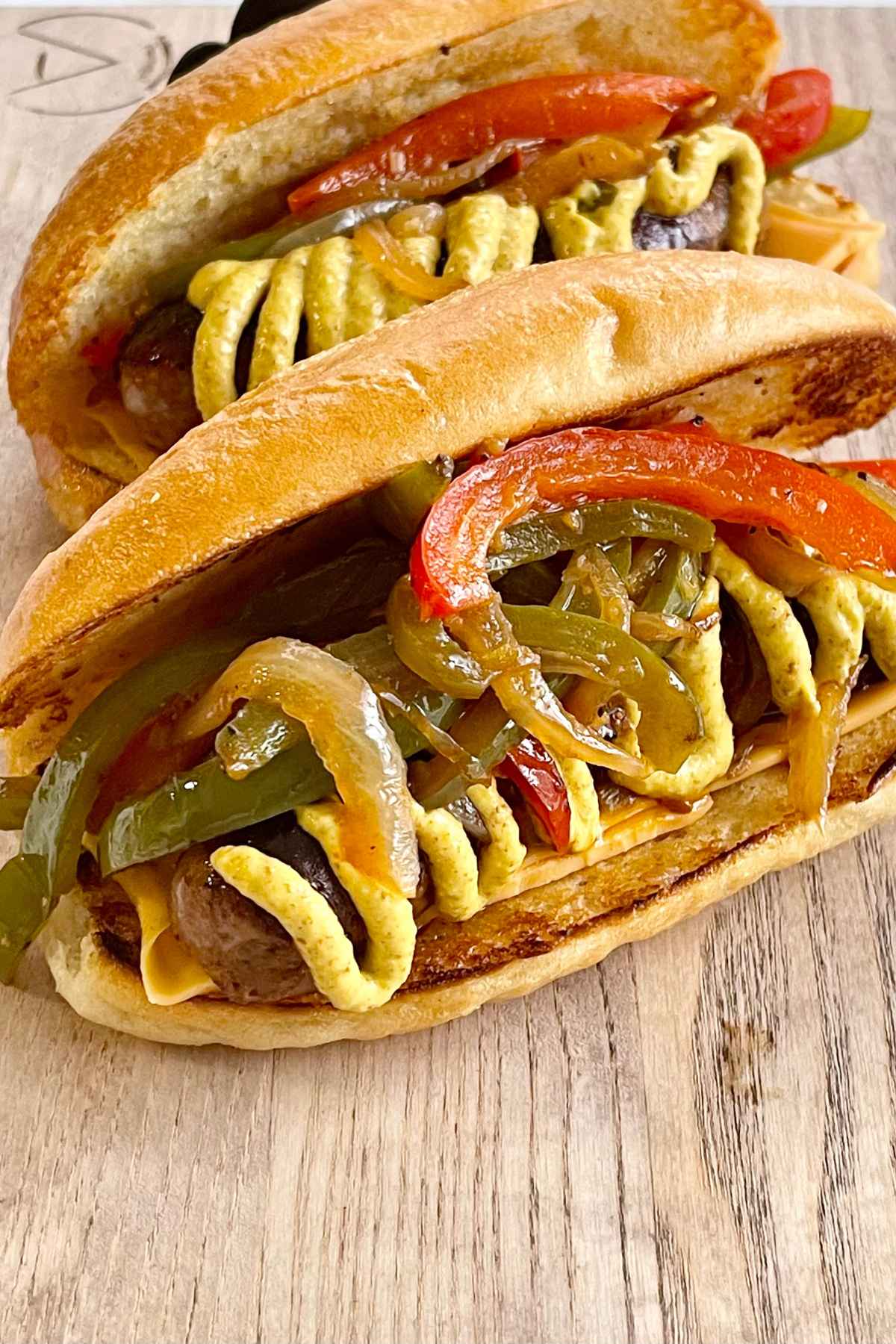Whole Italian sausages in a toasted hoagie roll topped with mustard, peppers, and onions.