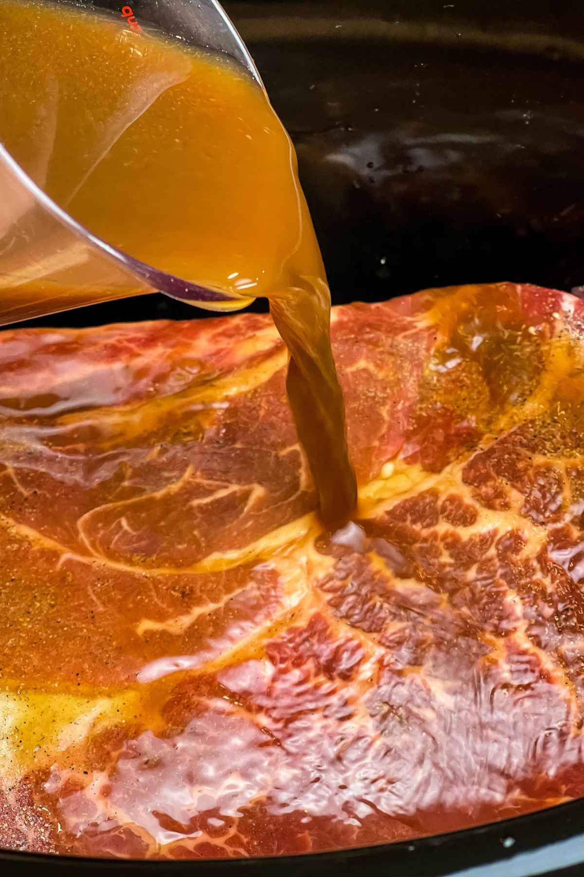 Pouring broth mixture over roast in slow cooker.