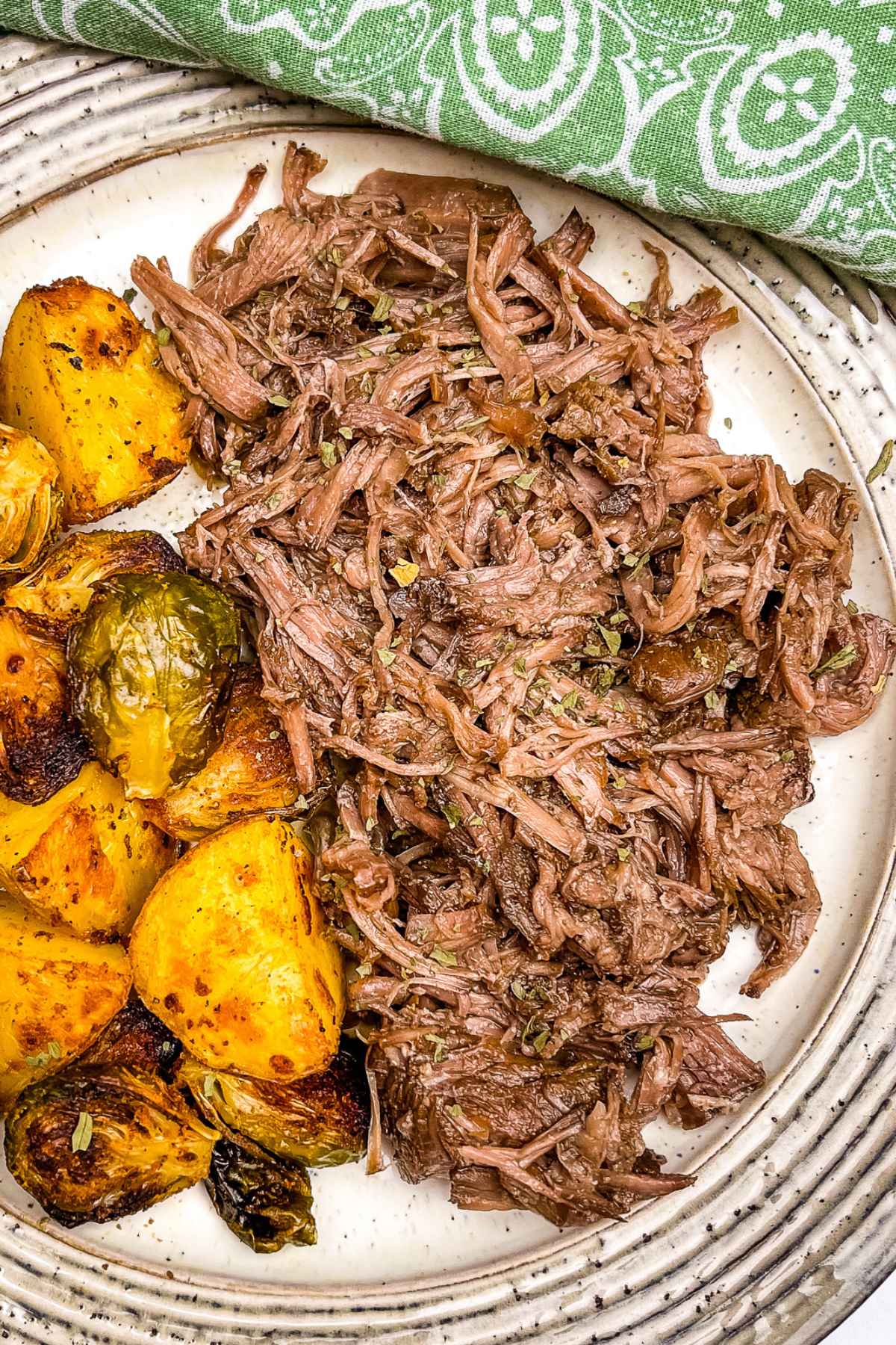 Shredded Beef on a plate with a side of roasted potatoes and brussels sprouts.