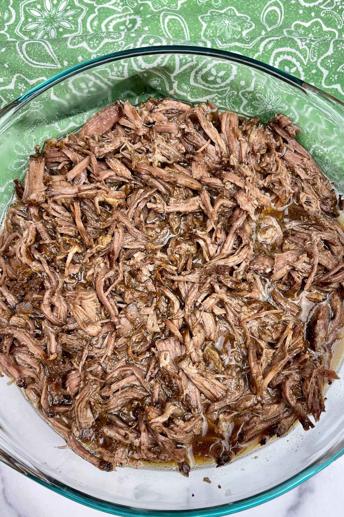 Shredded beef in a bowl with the juice from the roast.