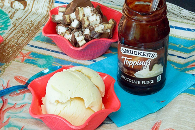 A scoop of vanilla bean ice cream in a sundae bowl with a jar of chocolate fudge behind the bowl.