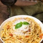 Angled image of Spaghetti Arrabiata in a pasta bowl with a glass of red wine.