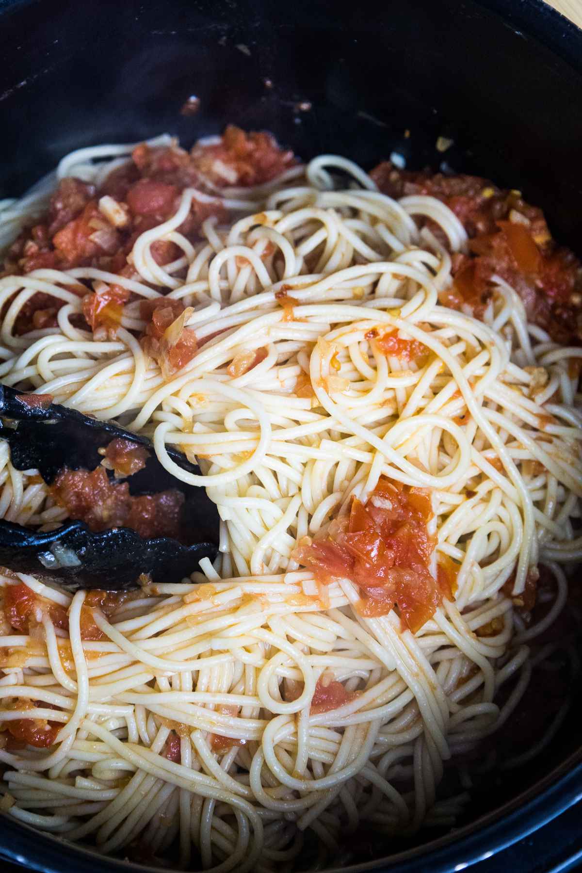 Tossing cooked pasta noodles with tomato sauce.