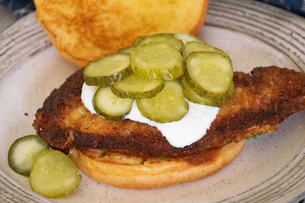 Open-faced Crispy Chicken Sandwich in a toasted bun with a pile of pickles on top.