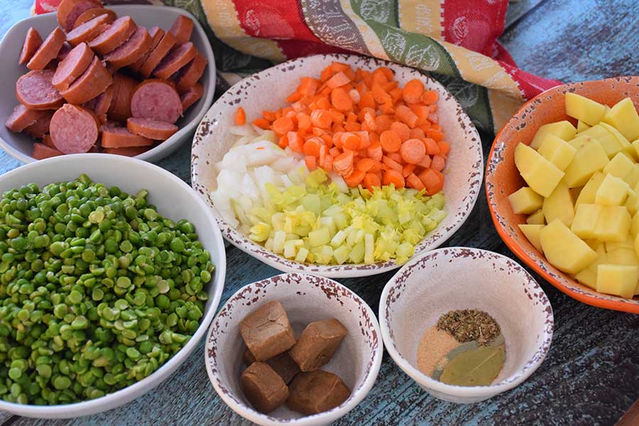 Ingredients for slow cooker soup recipe, split peas, bouillon cubes, herbs, diced potatoes, celery, onion, carrots, and slices of kielbasa sausage.