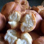 A tray of golden brown homemade buttermilk doughnuts with one deep fried doughnut broken in half to show the inside