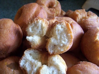 A tray of golden brown homemade buttermilk doughnuts with one deep fried doughnut broken in half to show the inside