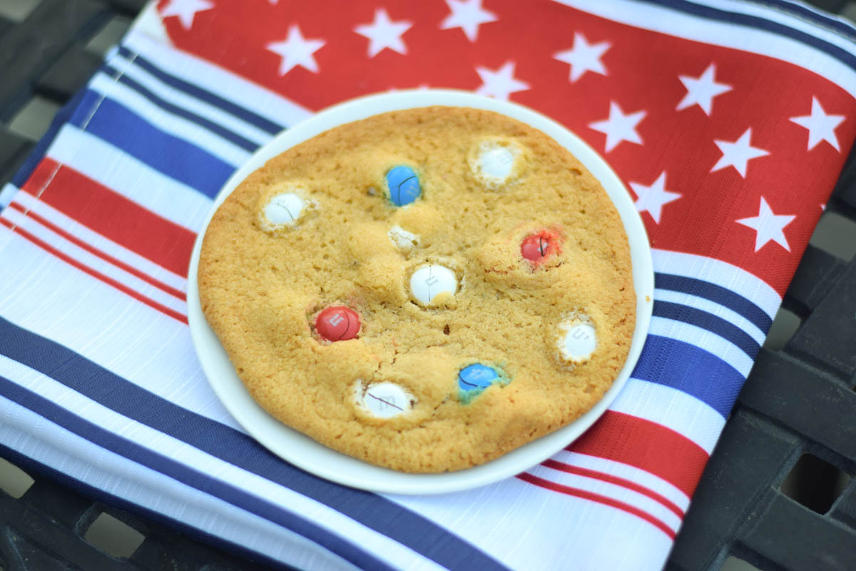One M and M cookie on a plate with red white and blue napkin.