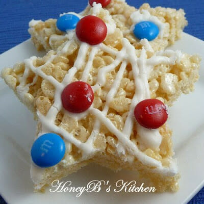 Two rice krispie treat stars on a white plate decorated with white chocolate drizzle and patriotic m&ms.