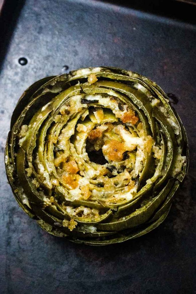 Artichoke stuffed with cheese and herb filling on a baking sheet before broiling