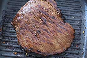 flank steak cooking on a grill pan