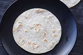 warmed corn tortilla on a black plate.