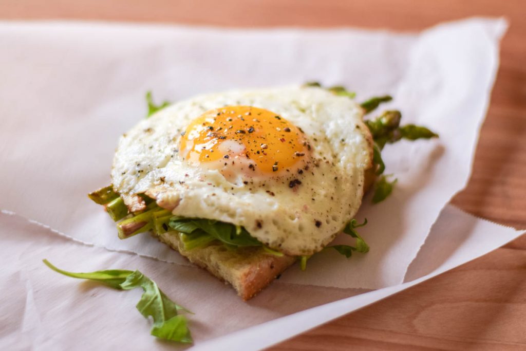 bottom layer of sandwich with cheese, asparagus, and fried egg on top
