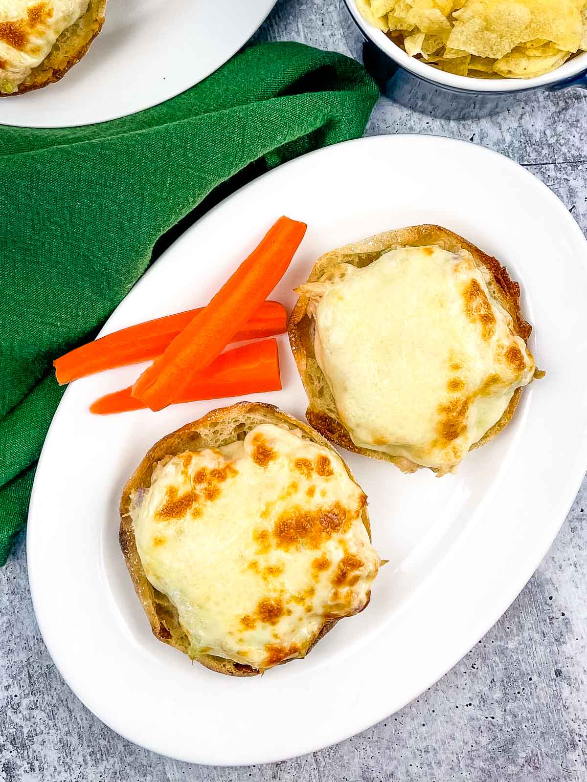 Overhead shot of English Muffin Tuna Melt with carrot sticks on a white plate.