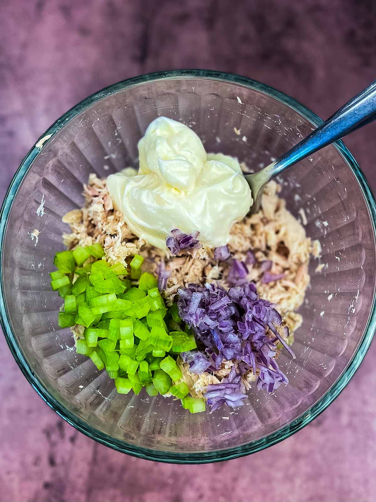 Tuna, mayonnaise, diced red onion, and celery in a mixing bowl with a fork.