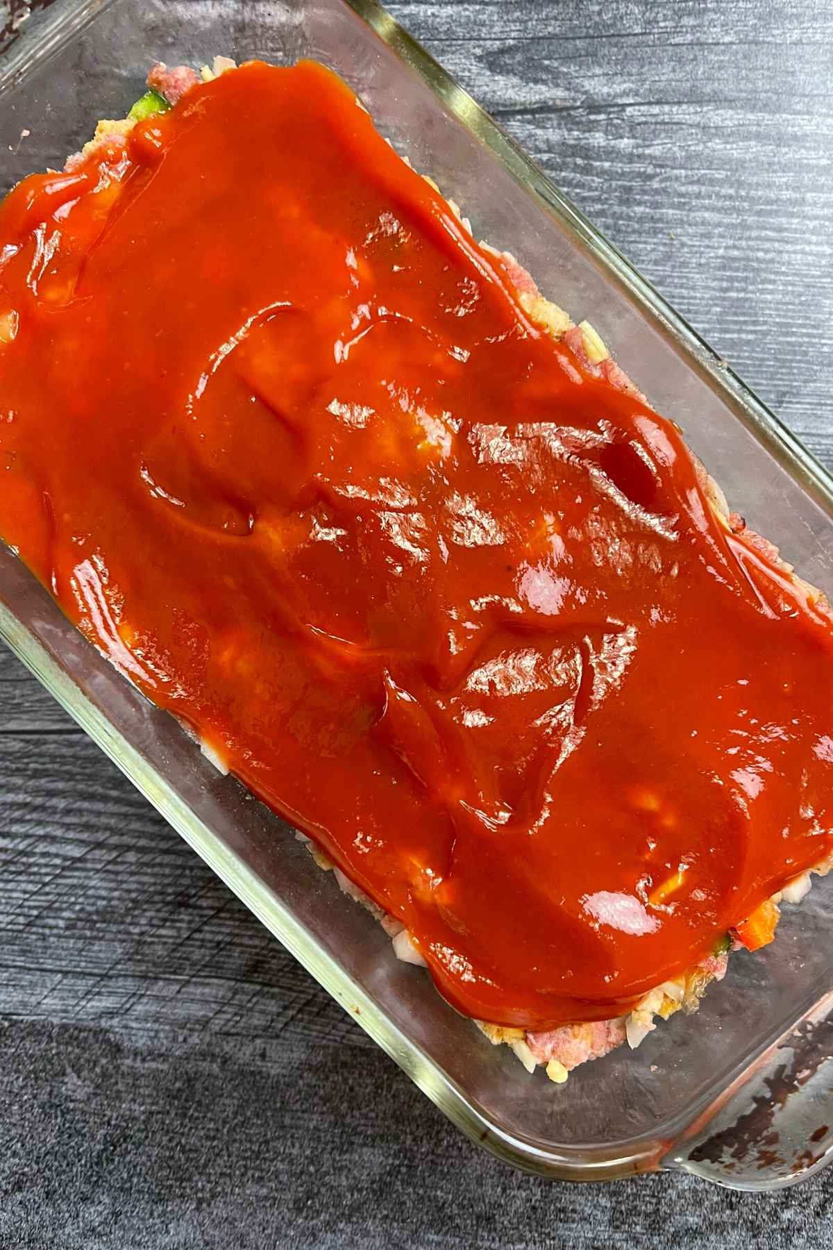 Overhead shot of unbaked meatloaf topped with ketchup.