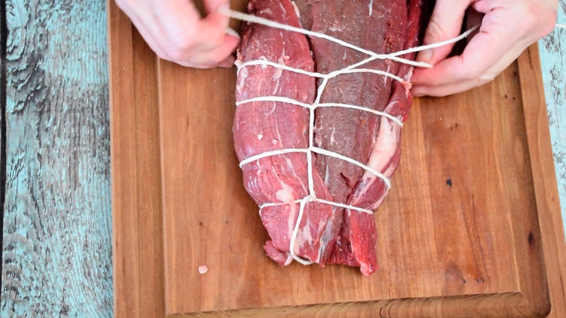 A pair of hands tying a Whole Beef Tenderloin Roast with kitchen twine.