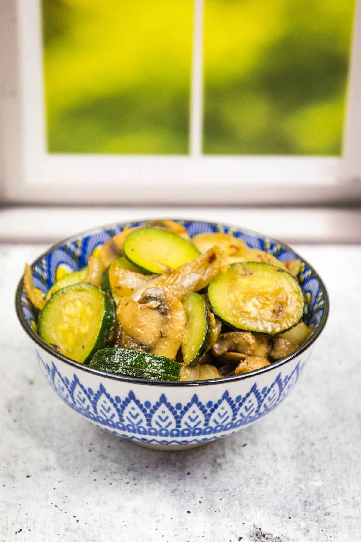 A patterned blue bowl filled with sauteed zucchini and mushrooms.