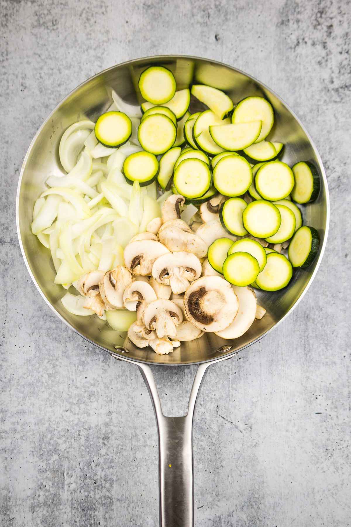 Skillet with raw zucchini, onions, mushrooms, and garlic.